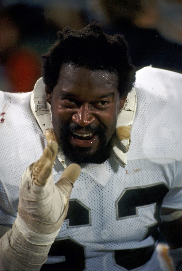 File photo: Oakland Raiders guard Gene Upshaw (63) smiles on the sideline in a white jersey with a taped left hand raised.