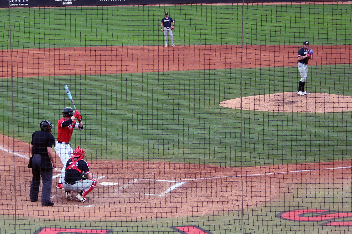 UNLV infielder Cooper Sheff (22) stands in the batter’s box with his bat raised as the pitcher sets on the mound, with the catcher and umpire behind home plate.