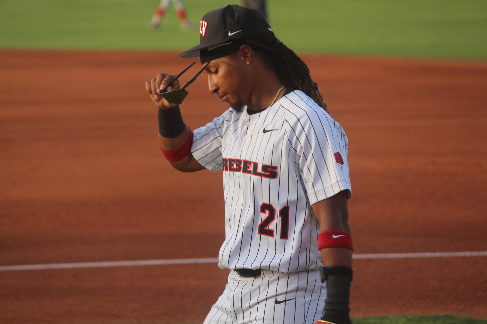 UNLV outfielder Nin Burns II (#21) lowers his sunglasses while standing on the infield dirt in a pinstriped Rebels uniform.