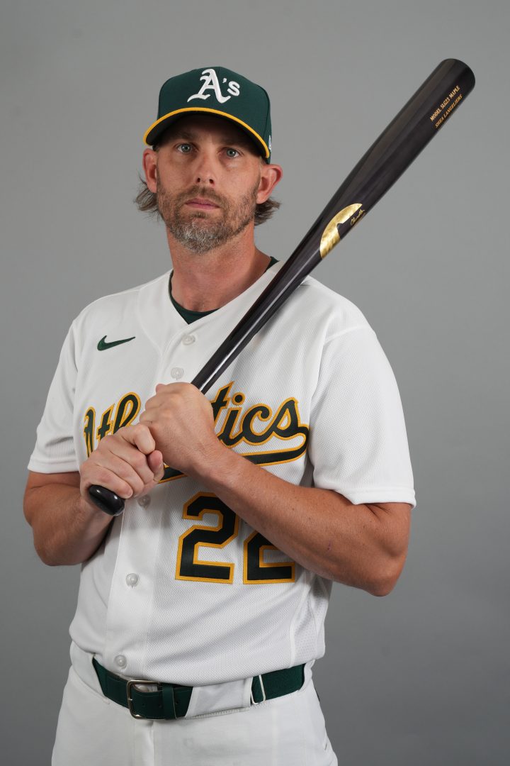 Athletics second baseman Jeff McNeil poses during team photo day holding a bat over his shoulder while wearing the A’s white home uniform and green cap.