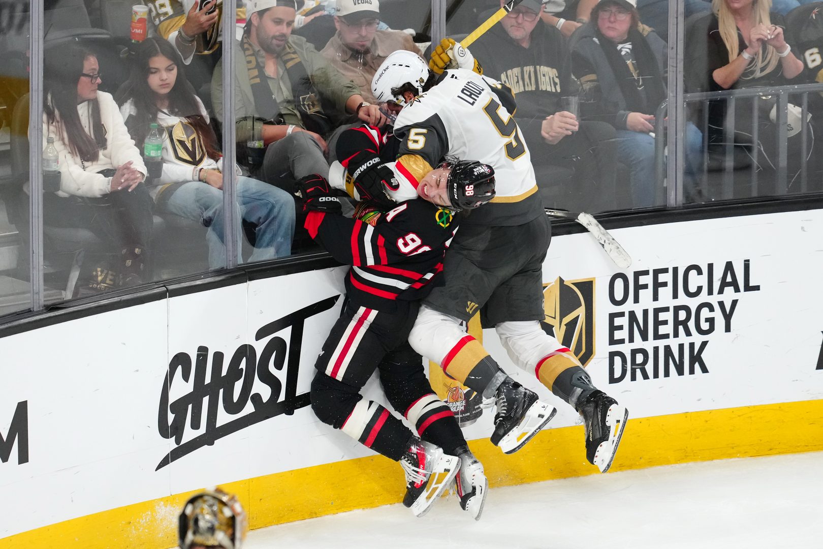 Vegas Golden Knights defenseman Jeremy Lauzon (5) delivers a check on Chicago Blackhawks center Connor Bedard (98) along the boards during the third period at T-Mobile Arena in Las Vegas on March 14, 2026.