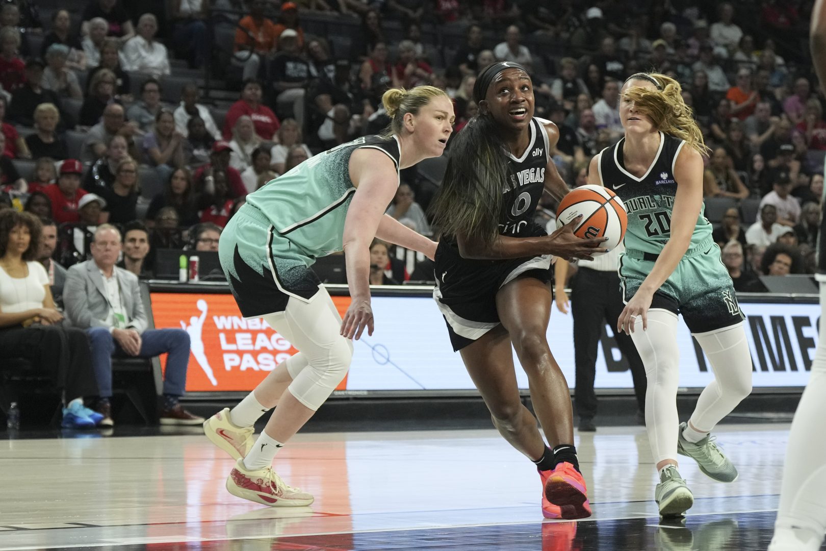 Jackie Young drives past Emma Meesseman and Sabrina Ionescu during a Las Vegas Aces game.