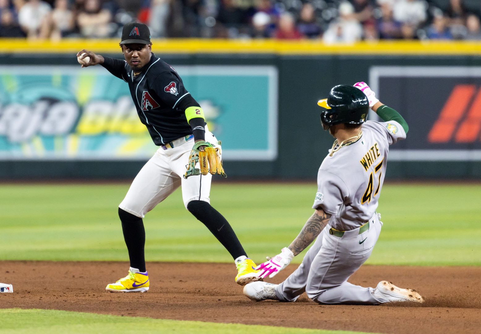 Diamondbacks shortstop Geraldo Perdomo turns a double play as Athletics runner Tommy White slides into second base.