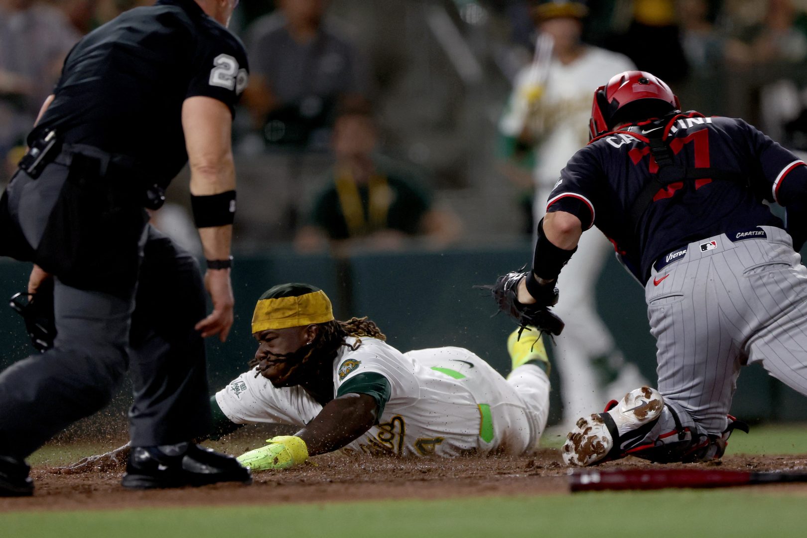 Athletics right fielder Lawrence Butler slides ahead of Minnesota Twins catcher Victor Caratini